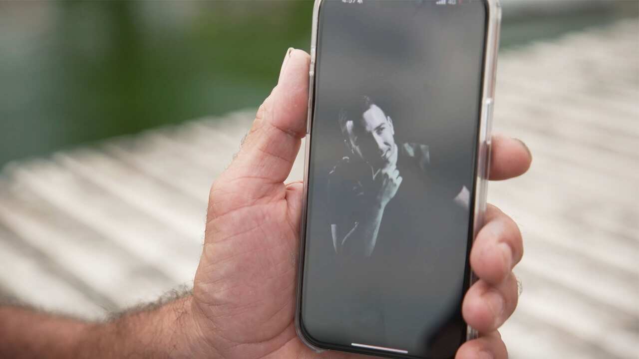 A hand holding a phone showing a black and white photo of a young man