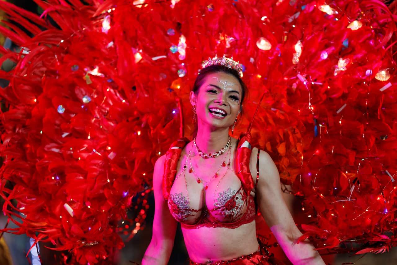 A woman smiles at the camera, weaing a large red feathered costume.