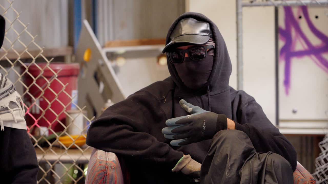 A group sit in a shed with graffiti. 
