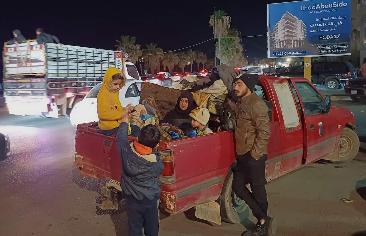 A family sitting in the back of a red ute as cars pass by.