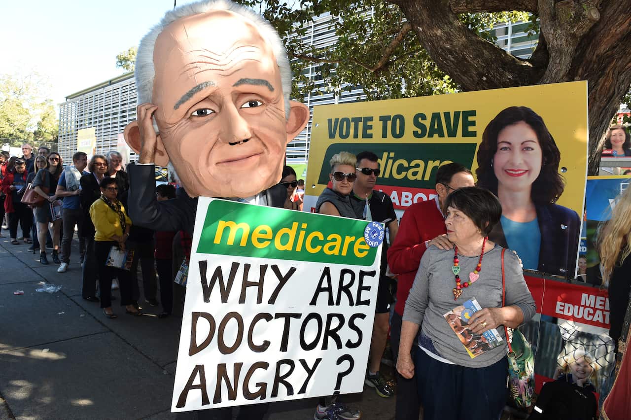 A protester wearing a giant puppet head depicting Prime Minister Malcolm Turnbull holds a sign criticising the government's policy on Medicare. 