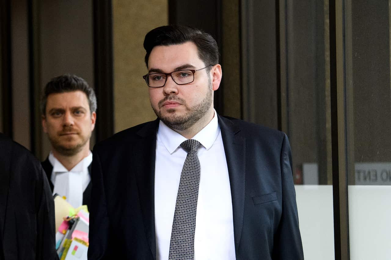 A man in a blue suit and tie, wearing glasses.