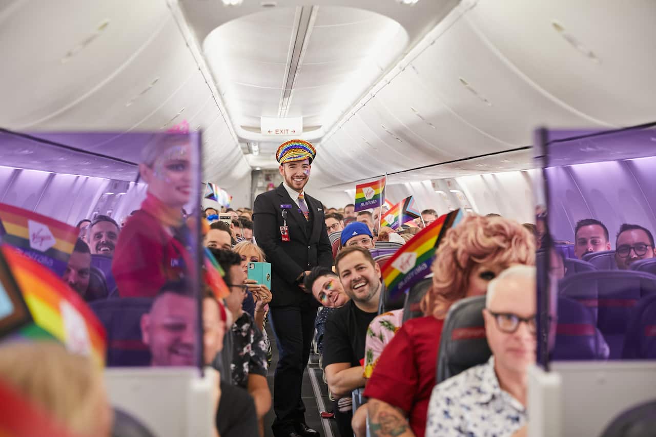 The interior of a plane with a flight steward in the aisle and passengers waving pride flags from their seats.