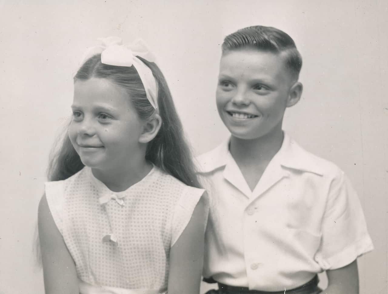 A black and white childhood portrait of a young boy and girl smiling.