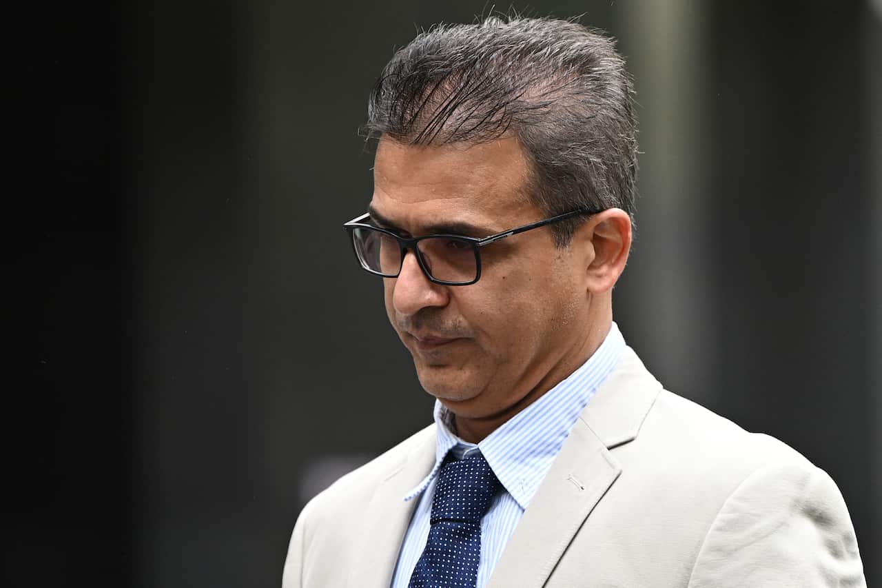 A man wearing a suit, tie, and glasses standing outside.