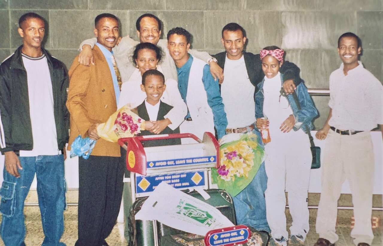 A young boy pushing an airport trolley is surrounded by people.