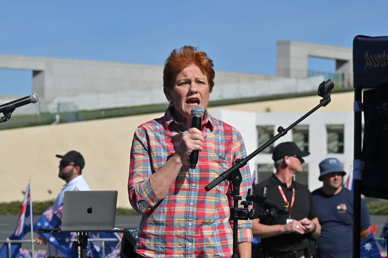 A woman wearing a plaid shirt speaking into a microphone.