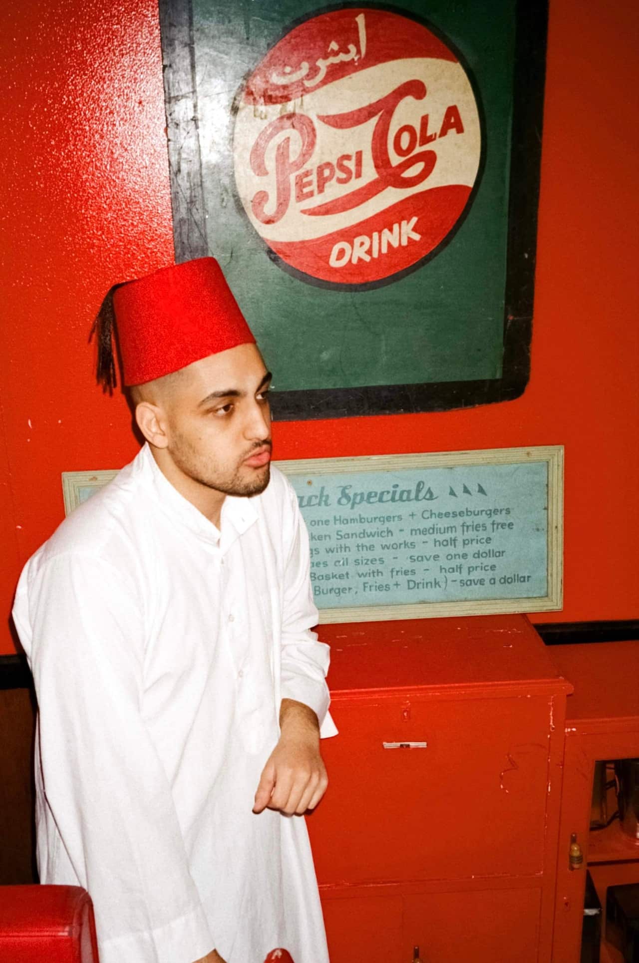 Man in front of a Pepsi sign wearing a tarboosh.