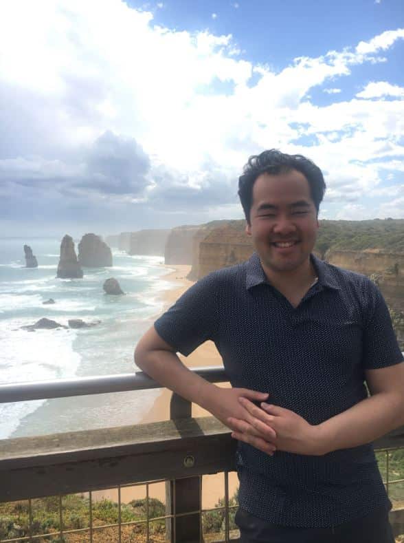A man smiles as he poses in front of a beach