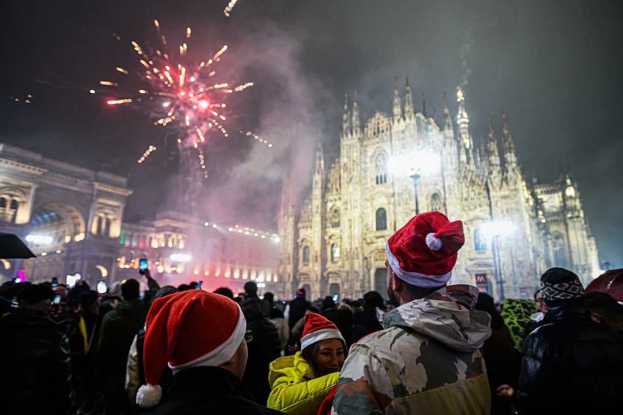 A crowd of people in warm clothes and Santa Claus hats celebrate the new year in Italy's Milan