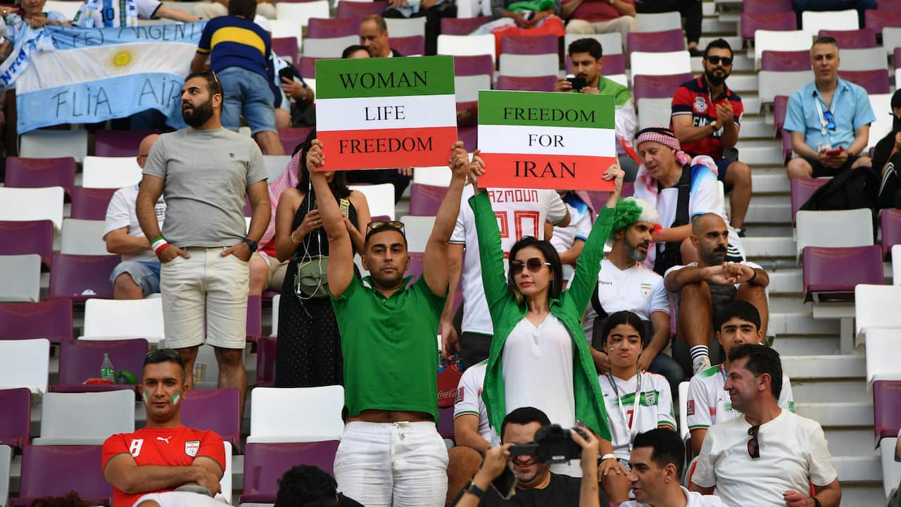 Fans in football stadium holdings signs which read 'WOMEN LIFE FREEDOM' with Iranian colours.