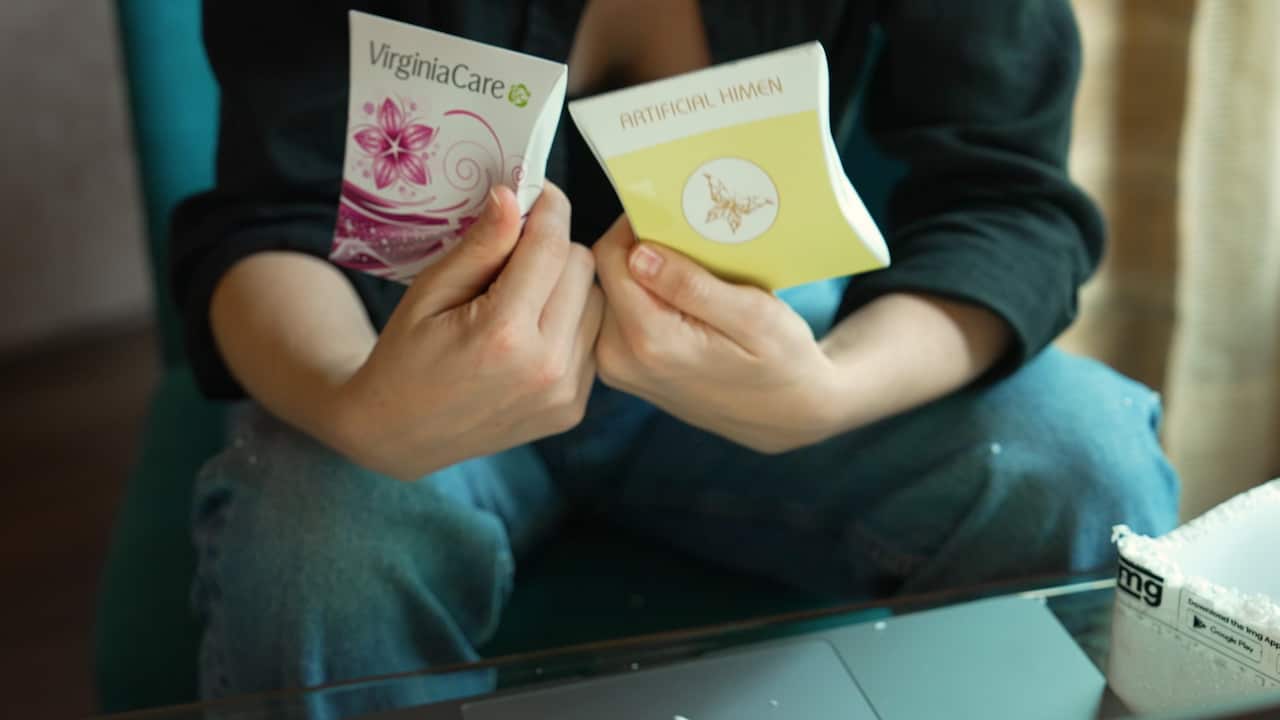 A woman's hands holding up two small packets, one with the label VirginiaCare and a pink flower, and a yelllow one with the label Artificial Himen.