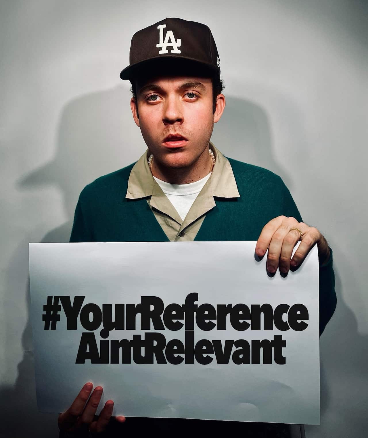 A young man holding a sign reading #YourReferenceAintRelevant