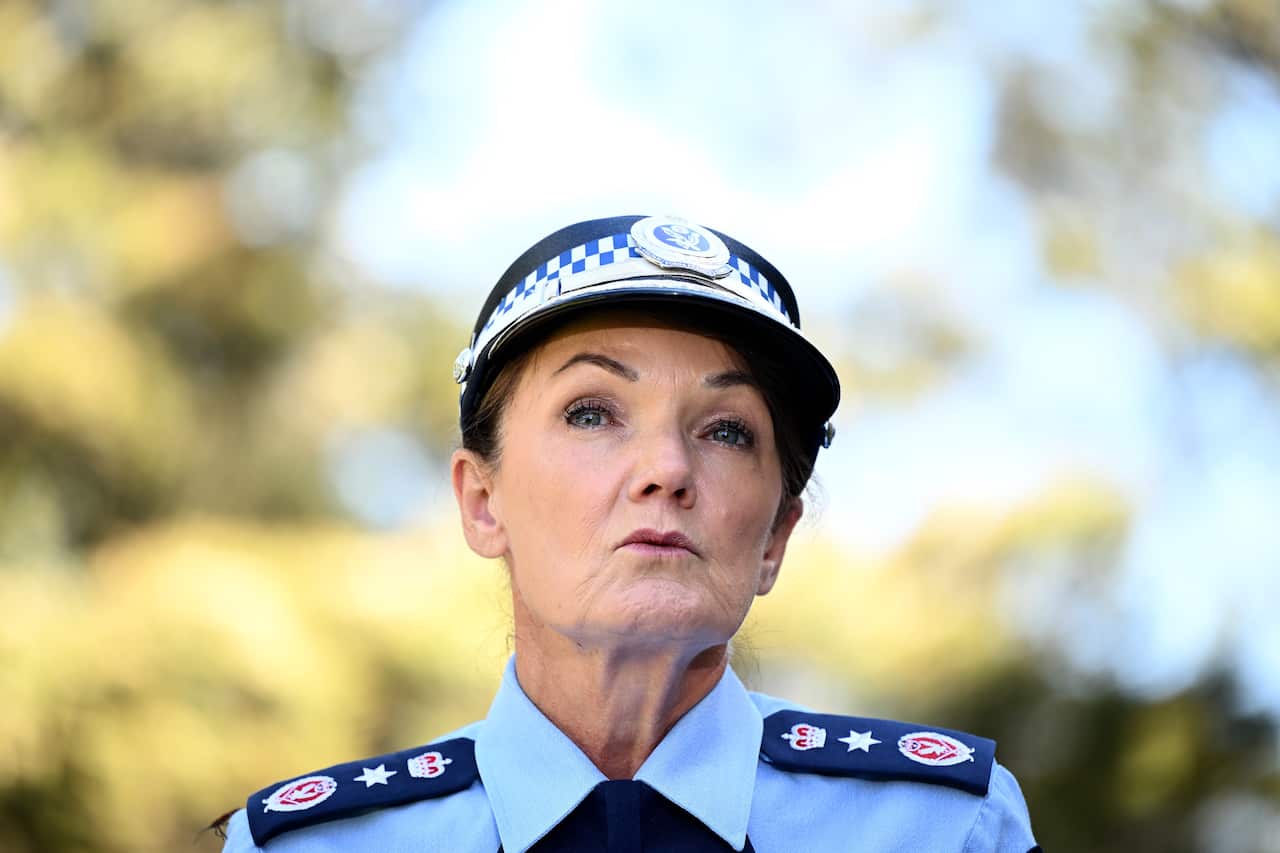 A woman wearing a police uniform speaks in front of green trees.