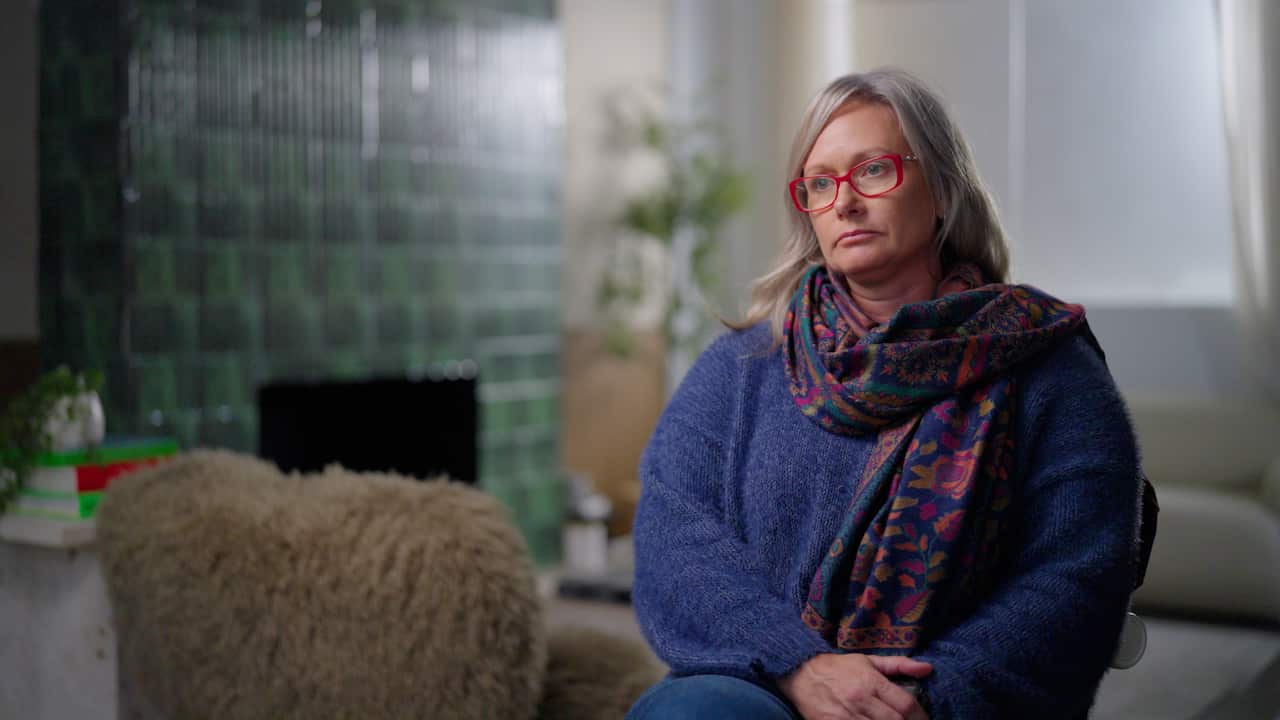 A woman wearing a scarf and red glasses sits in a chair.