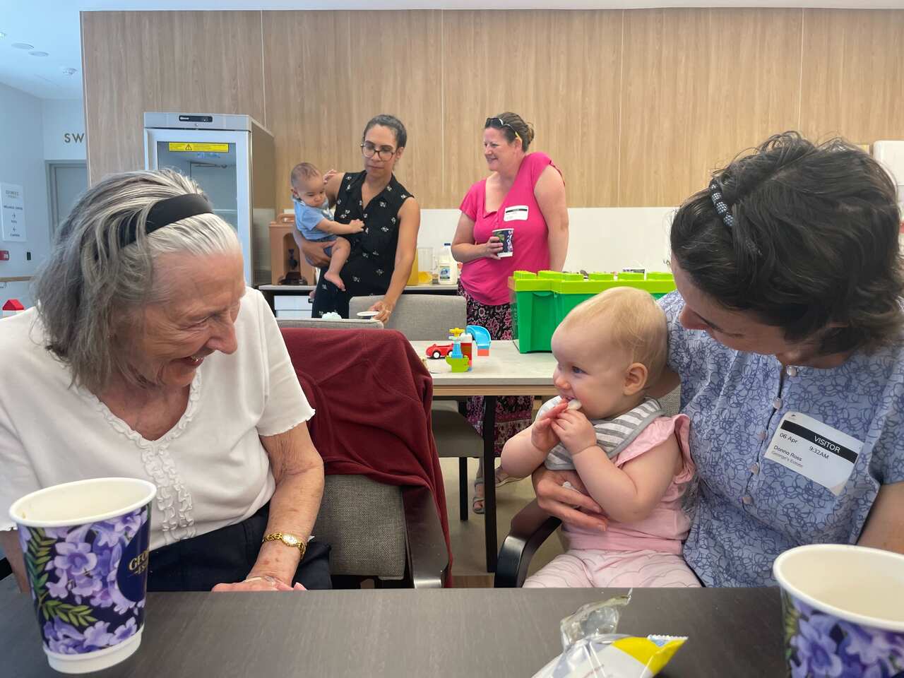 A mother holds her baby girl, laughing, with an older woman. 