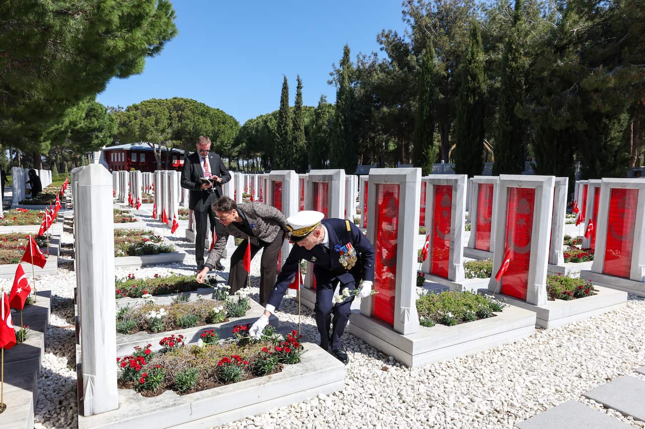 Military personnel places red carnations in a cemetery.