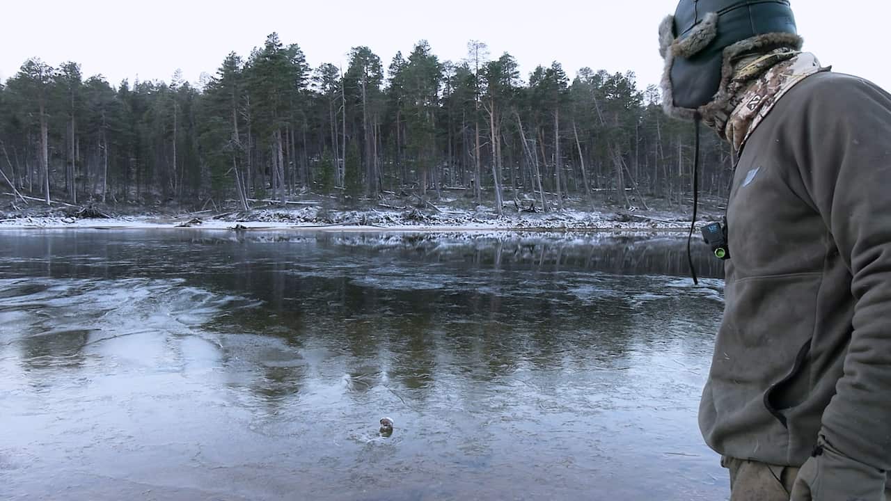 A man in winter clothing watches a frozen lake in a rural landscape.