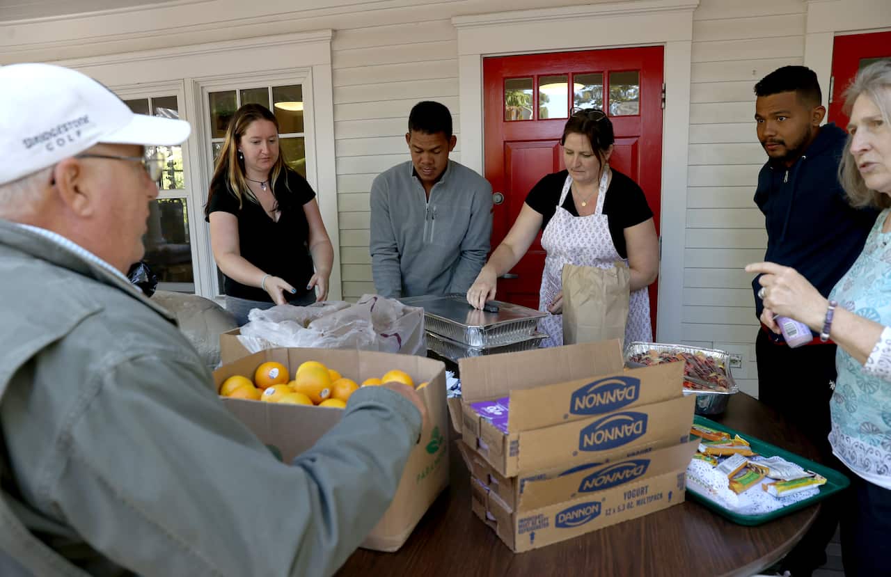 A group of people stand around a table with boxes of food on it