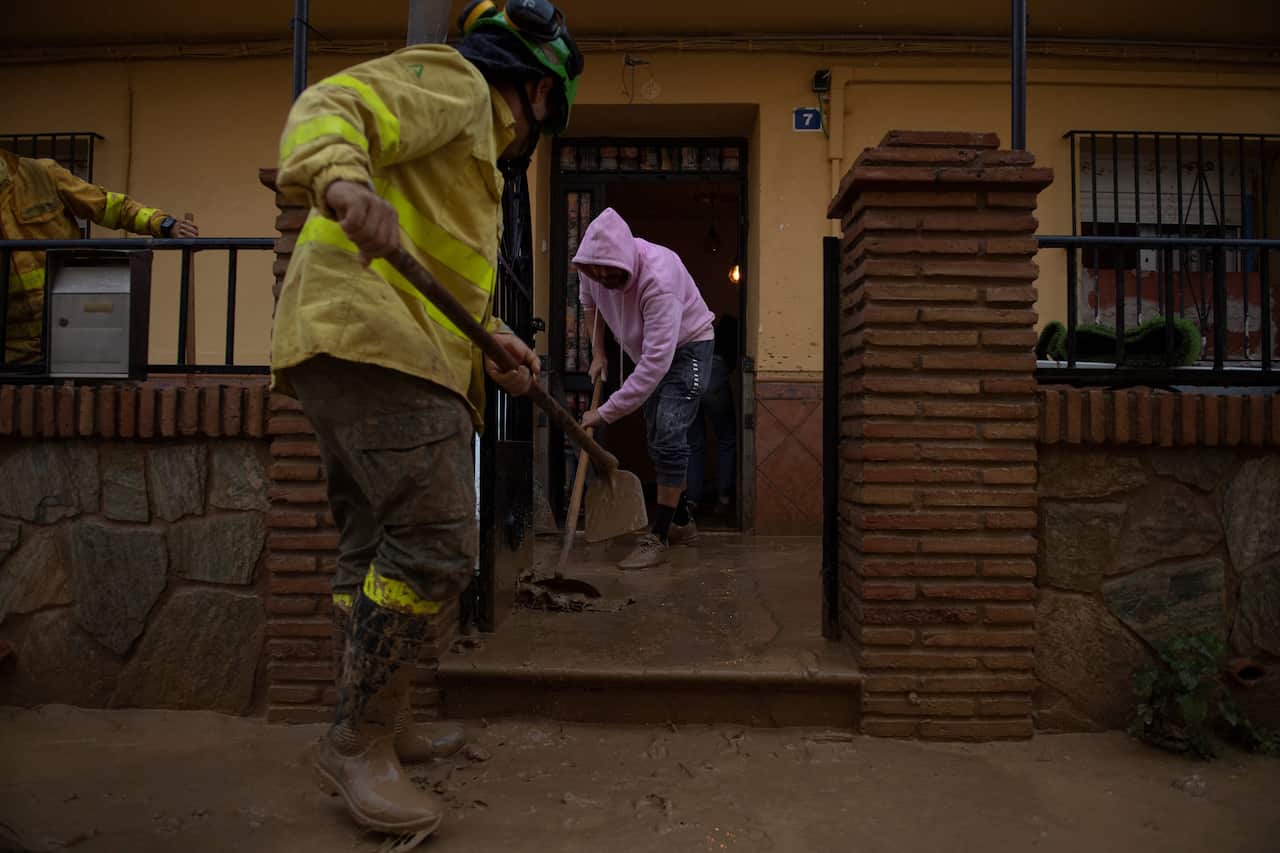 Two people sweep mud from out of the front of a house
