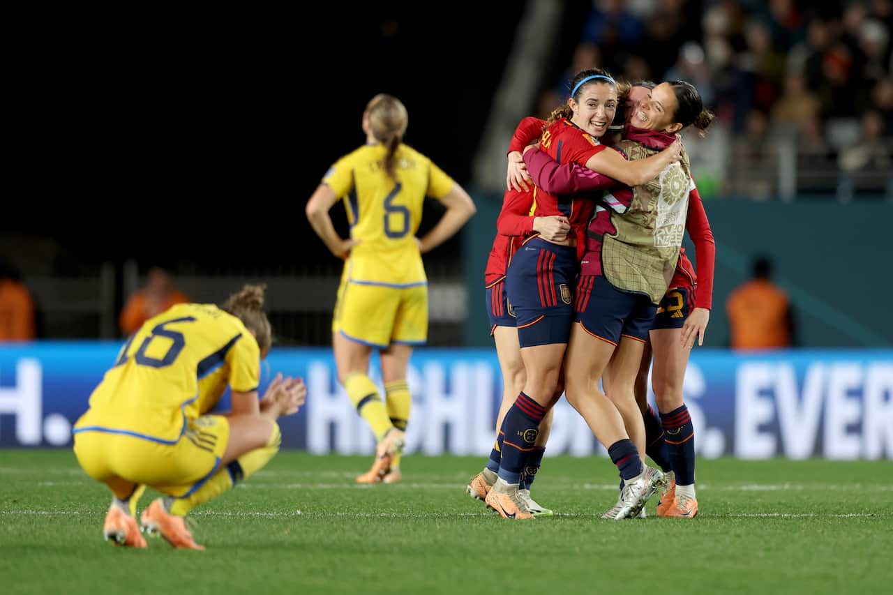 Spanish players are seen hugging and cheering while a Swedish player is crouched on the ground.