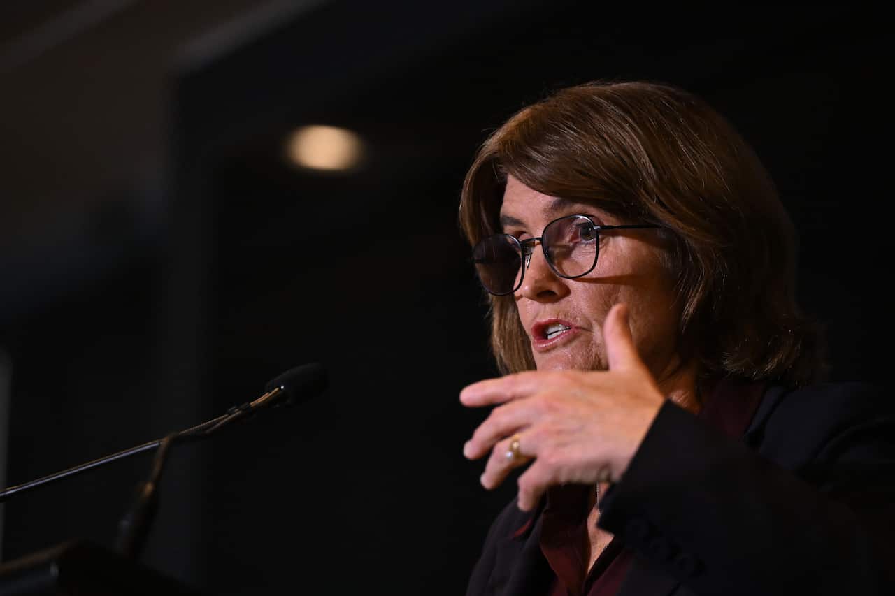 Michele Bullock speaking at a microphone. Her hand is raised.