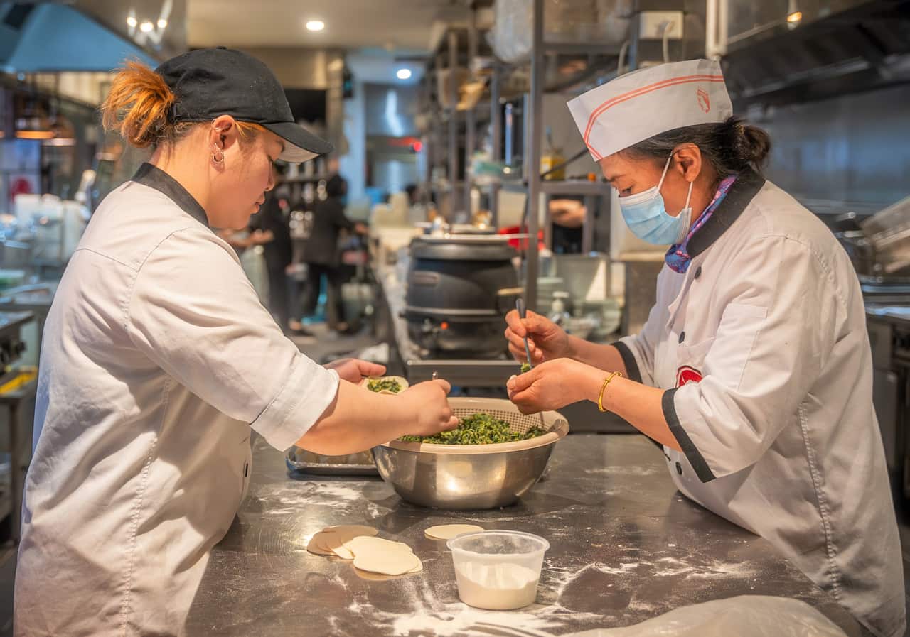 Two cooks in white uniforms prepare food in a restaurant kitchen.
