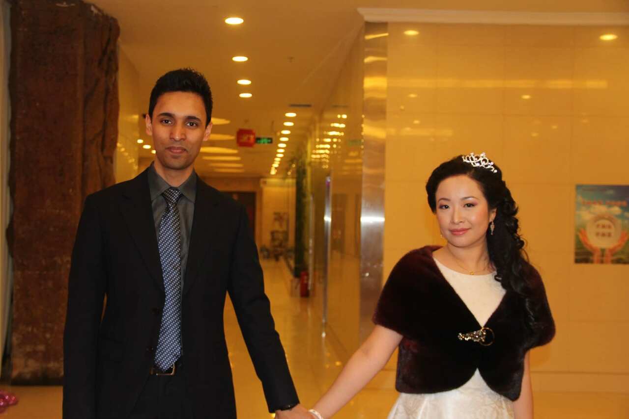 A man in a black suit and blue tie holds hands with a woman in a dress. 