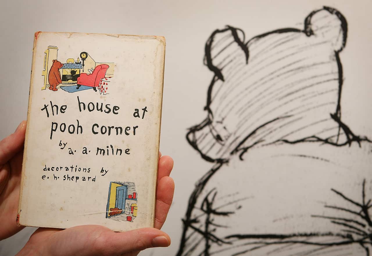 An illustration of Winnie-the-Pooh behind a hand holding a book titled The House at Pooh Corner.