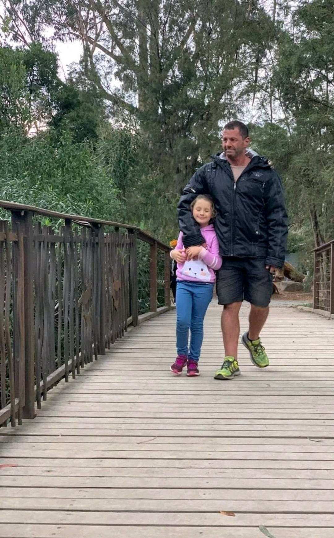 A man and his daughter walk happily across a bridge together.