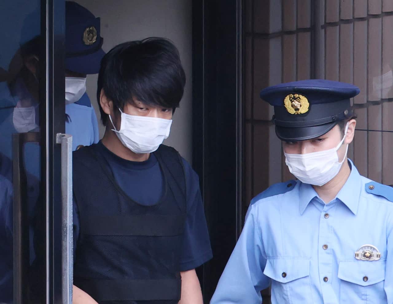 A Japanese man wearing a face mask is escorted by a police officer