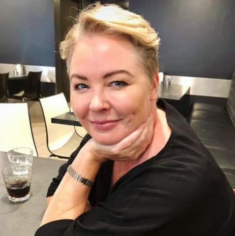 A woman with short blonde hair sits at a table at a café, wearing a black top