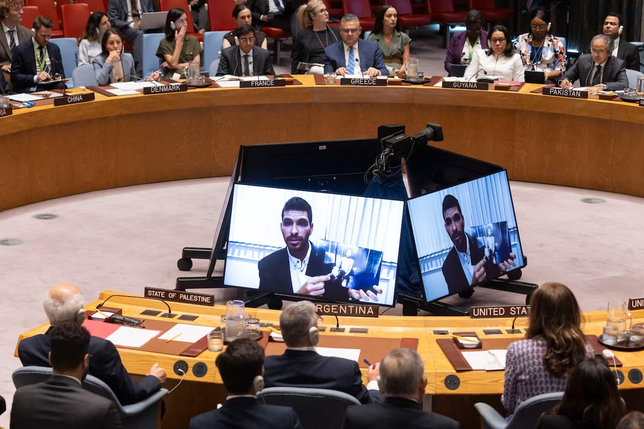 A man beamed on large monitors in front of people sitting in a conference room.
