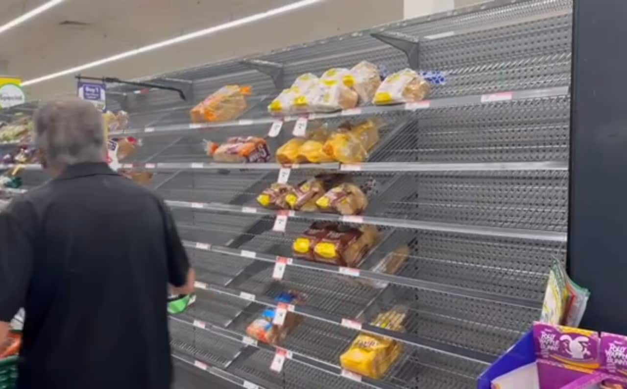 A man with a shopping trolley walks past mostly empty shelves of bread.