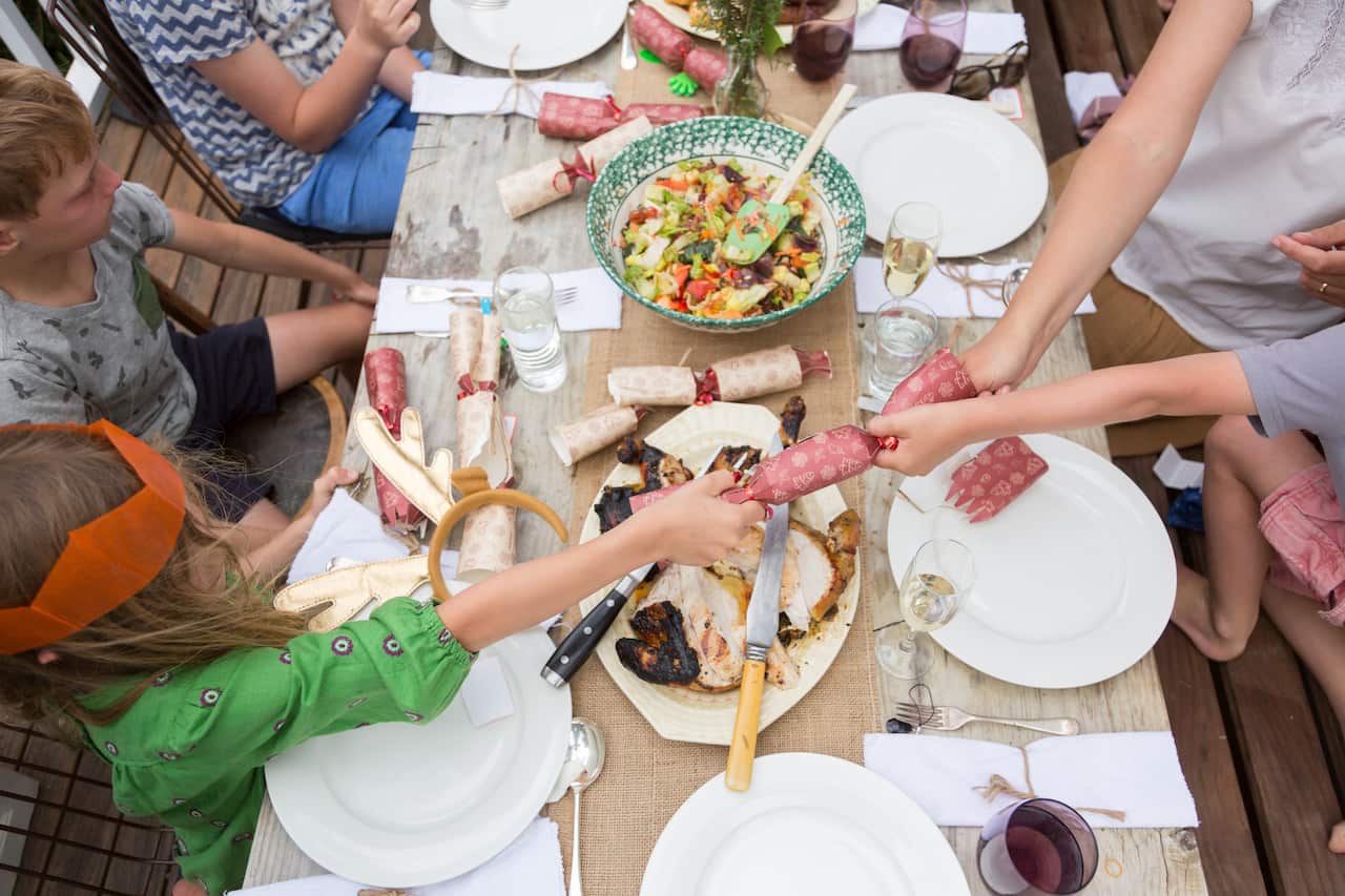 A family sit outside eating Christmas lunch and pulling Christmas crackers