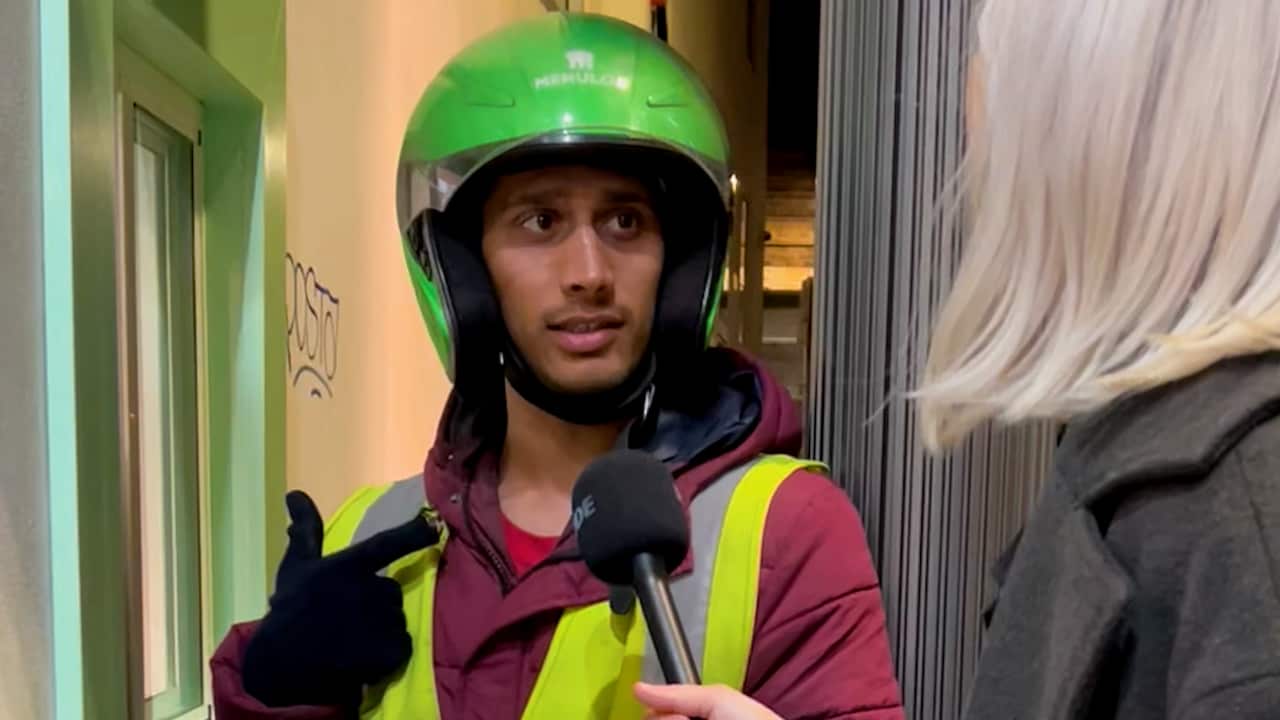 Food delivery rider wearing green helmet, talking to a blonde woman while waiting to collect an order.