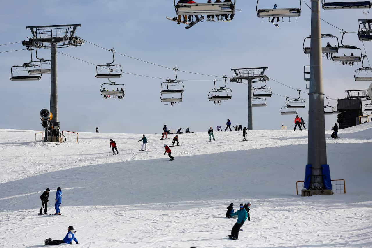 Skiers and snowboarders on a ski run at Mount Buller. Ski lifts operate above them.