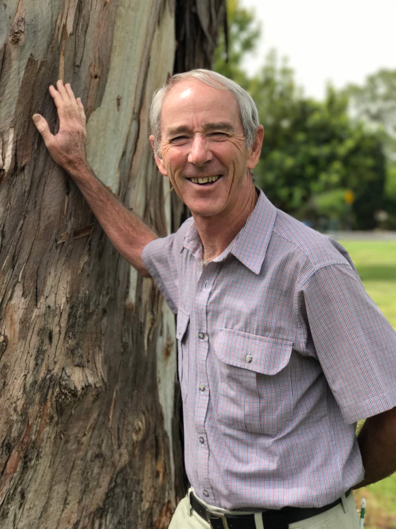 A man smiling while touching a tree.