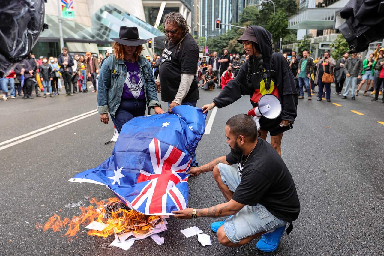 Four people gather in the street and burn an Australian flag
