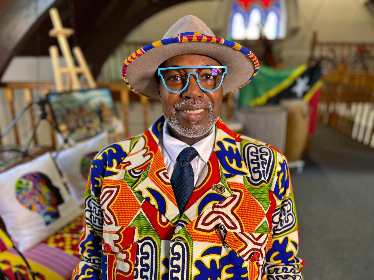 A man in a colourful jacket, blue-rimmed sunglasses and a straw hat