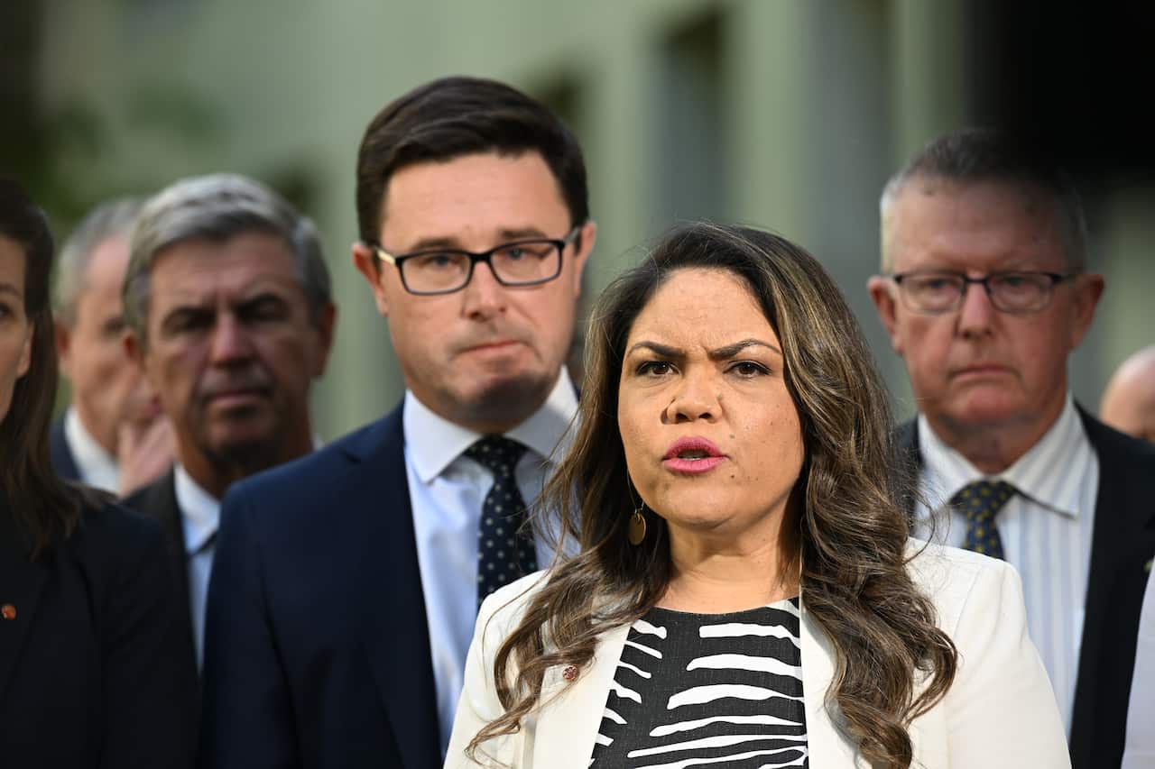 Jacinta price is speaking in a black and white top and a white blazer over the top, with some nationals politicians in suits behind her. 