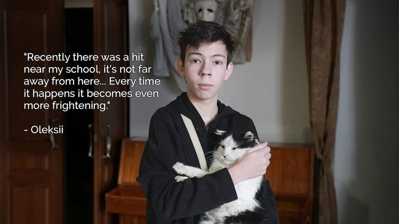 A 16-year-old boy holds a cat in his arms while standing inside.