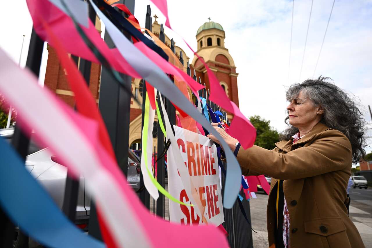 A woman tying a colourful ribbon to a fence.