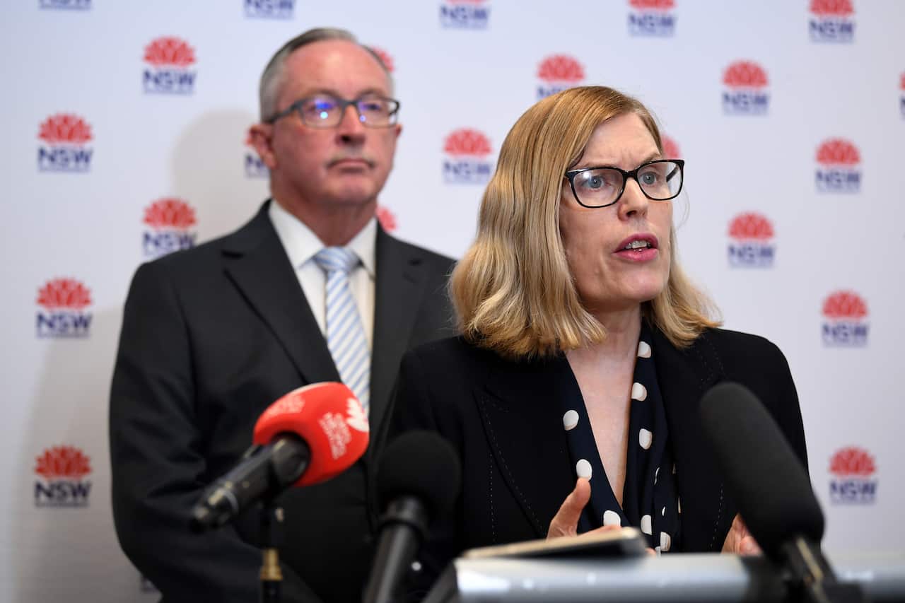 Dr Kerry Chant with Brad Hazzard in the background speaking at a podium.