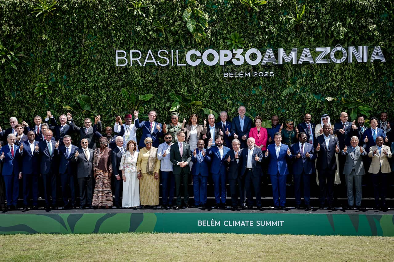 A large group of people stand on tiered stands in front of a sign that reads 'Brasil COP30 Amazonia'
