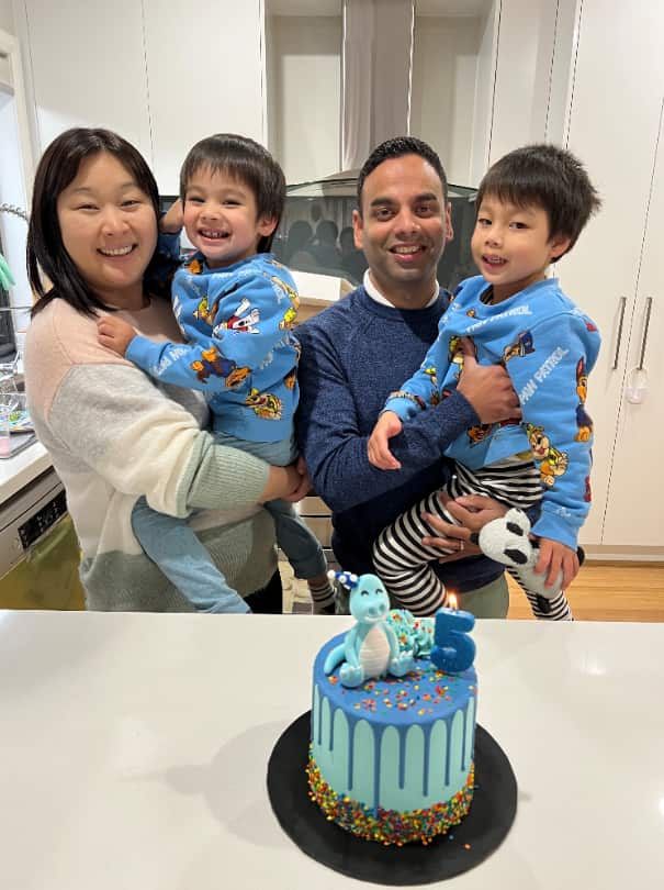 Lalith and his wife Louise holding their two children. They are standing behind a blue birthday cake. 