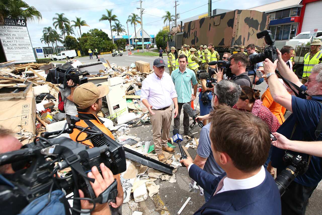 Prime Minister Scott Morrison is seen standing on a road amid flood-damaged items as he speaks to the media.