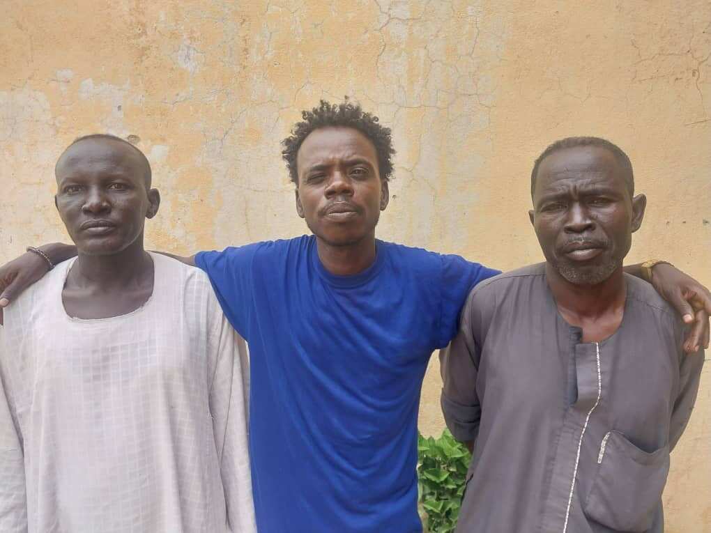 Three men standing against a wall.