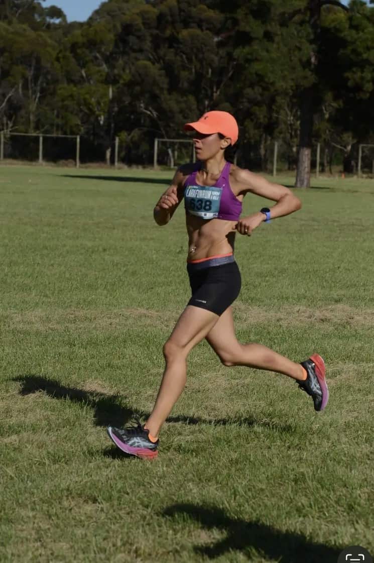 A woman wearing a competition bib runs on the grass 