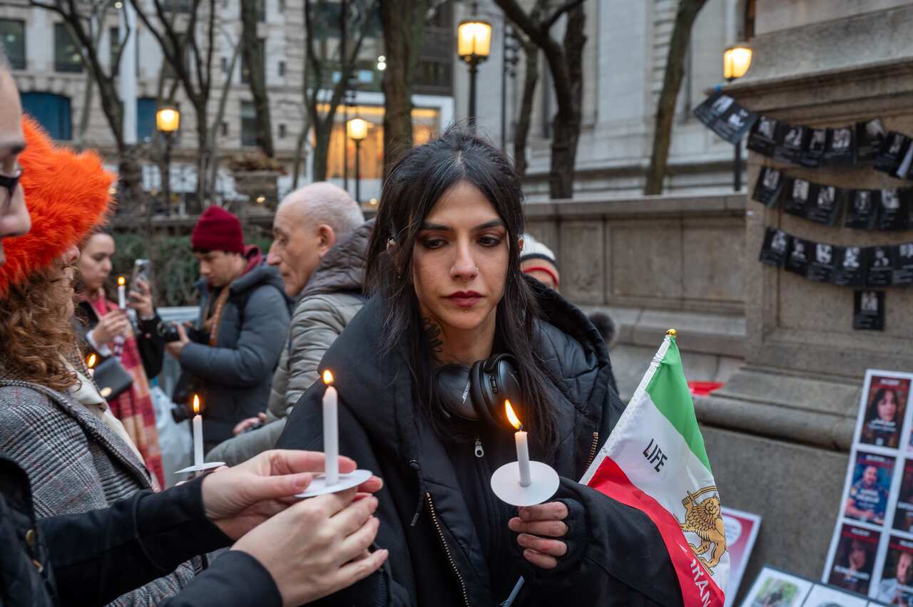 People on a street light candles while holding Iranian flags.